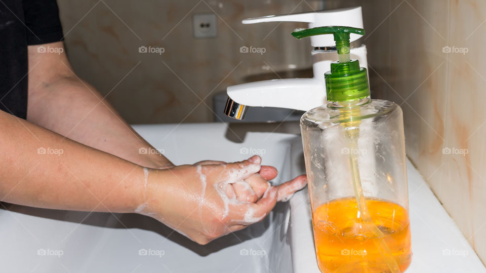 A man thoroughly washes his hands with soap in the bathroom, in a white washbasin with a white tap and antibacterial soap, makes a lot of foam and washes fingers and brushes after walking on the stree