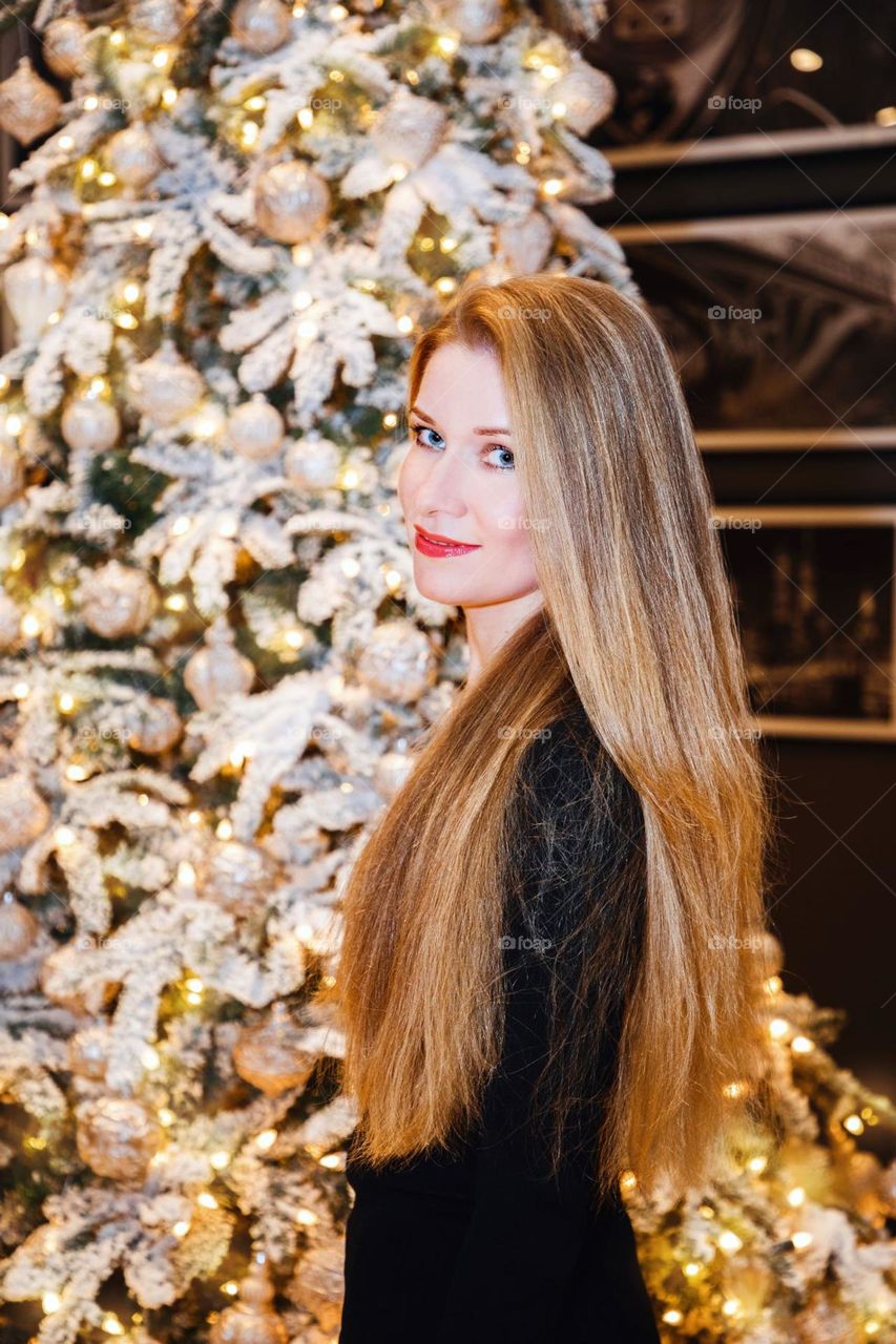 Pretty blonde girl with beautiful long hair standing near decorated tree