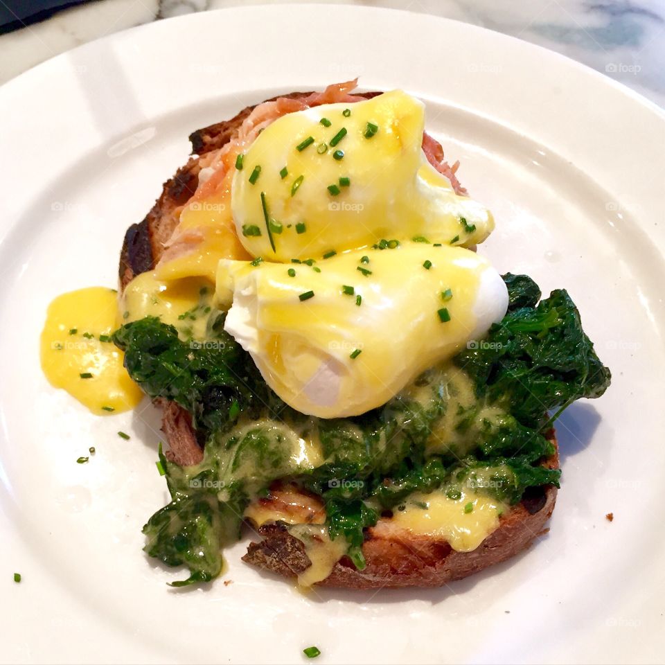 Eggs benedict with chives, hollandaise sauce on crusty bread with spinach and bacon