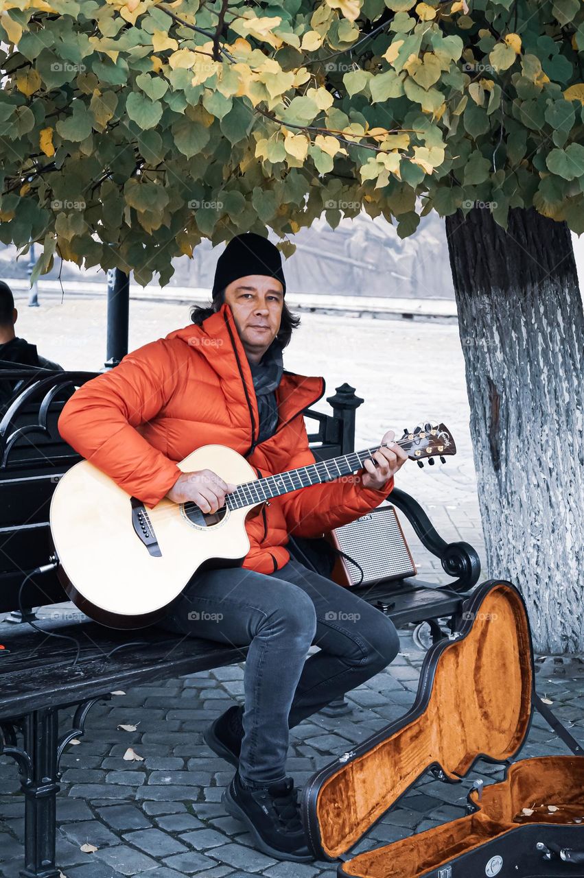 A man plays the guitar on the street of Krasnodar, attracting the attention of passers-by with a good melody and receives money