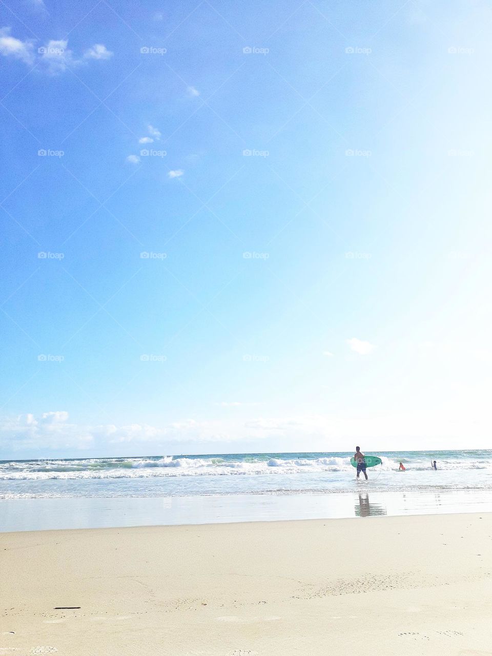 A surfer carries a surfboard into the ocean for a day of surfing at Indian Rocks Beach.