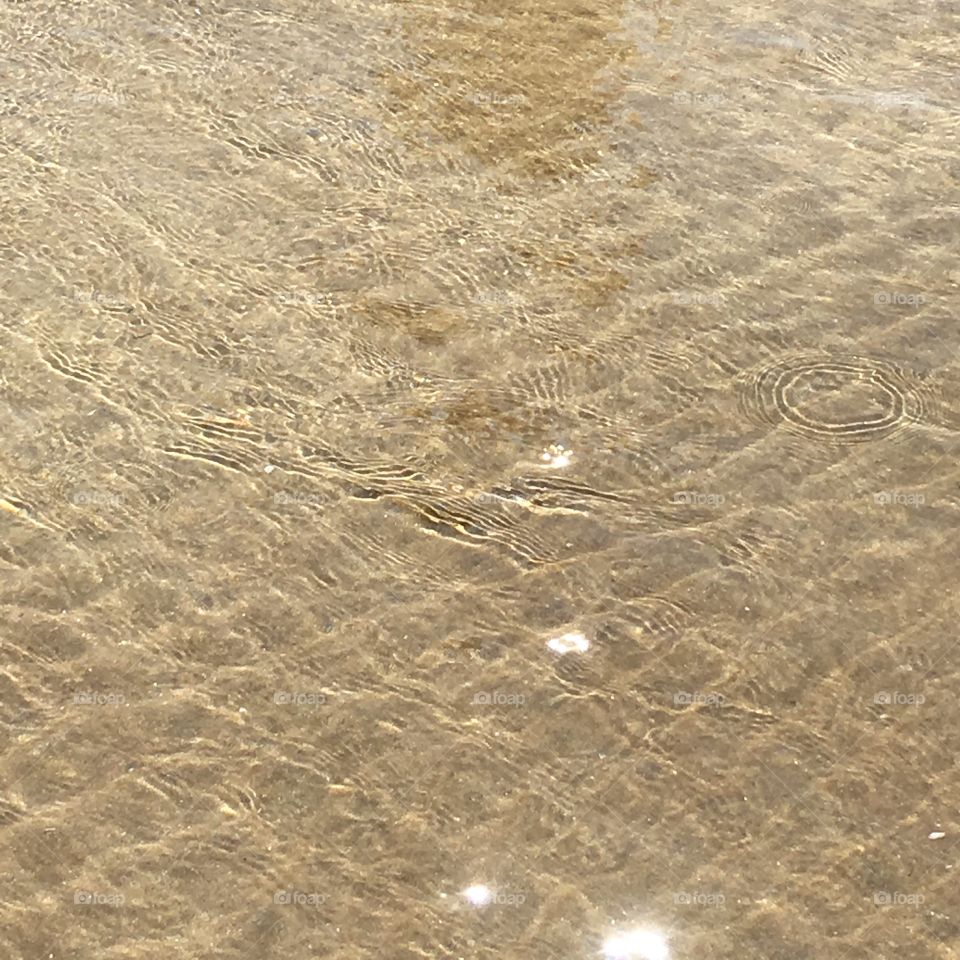 Reflection, light and natural patterns on the shallow water of Woolacombe beach, North Devon, England. Water is warm from the summer sun. 