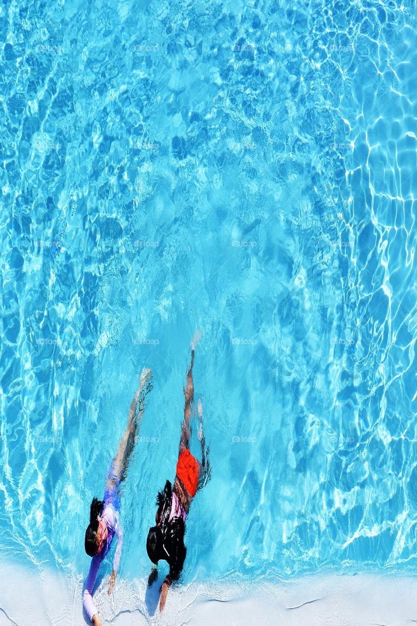 Two sisters on vacation enjoy a hot days worth of swimming in an emerald blue pool.