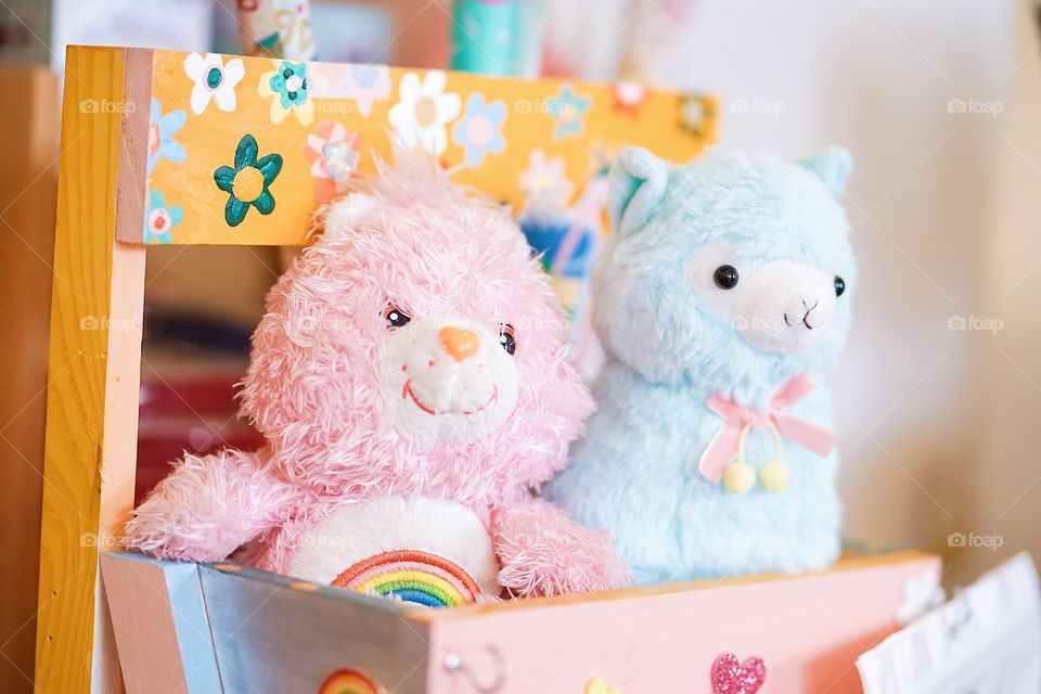 Bangkok, Thailand - April 30, 2018 : A photo of cute plush dolls or stuffed animals of a pink Care Bear and a cute alpaca doll are sitting on a wooden basket. Selective focus on the rainbow on a bear's tummy.