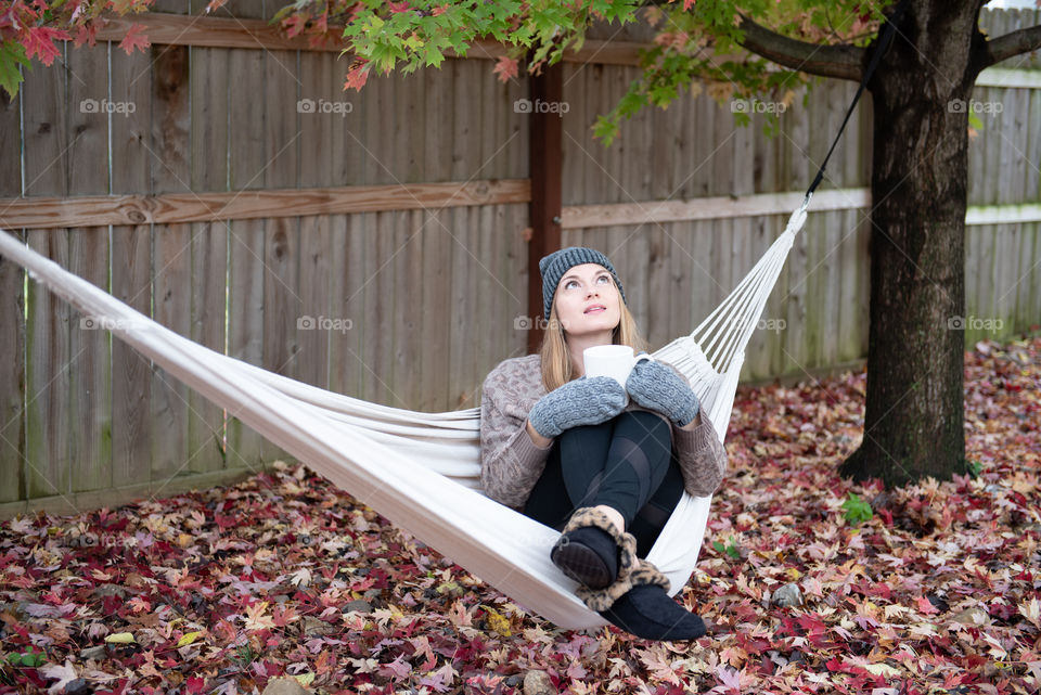 Young millennial woman sitting in a hammock and looking up during the fall