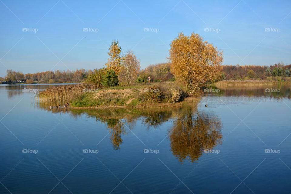 beautiful autumn landscape lake and person walking blue sky background, and reflection