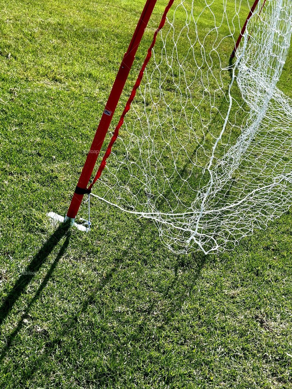 White netting and orange support pole on green grass field set up for recreational soccer game