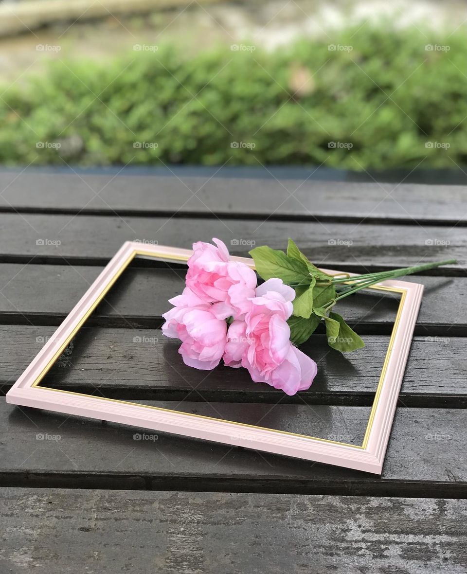 A bunch of beautiful pink flowers in between the pink photo frame on outdoor wooden table looks so pretty 😍