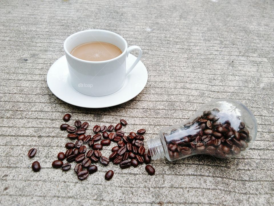 A White cup of coffee and coffee beans in glass bottle on concrete floor