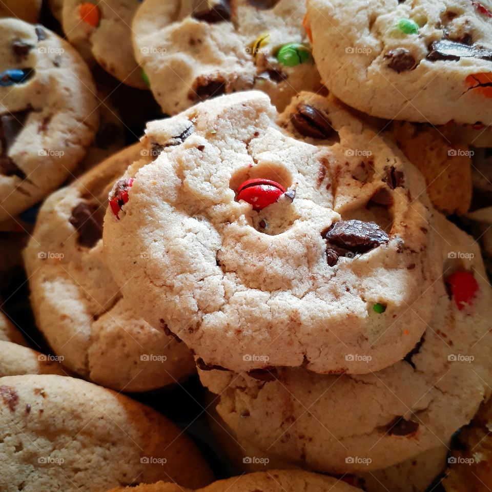 A box with many delicious chocolate chip cookies with candy coated chocolates in them.