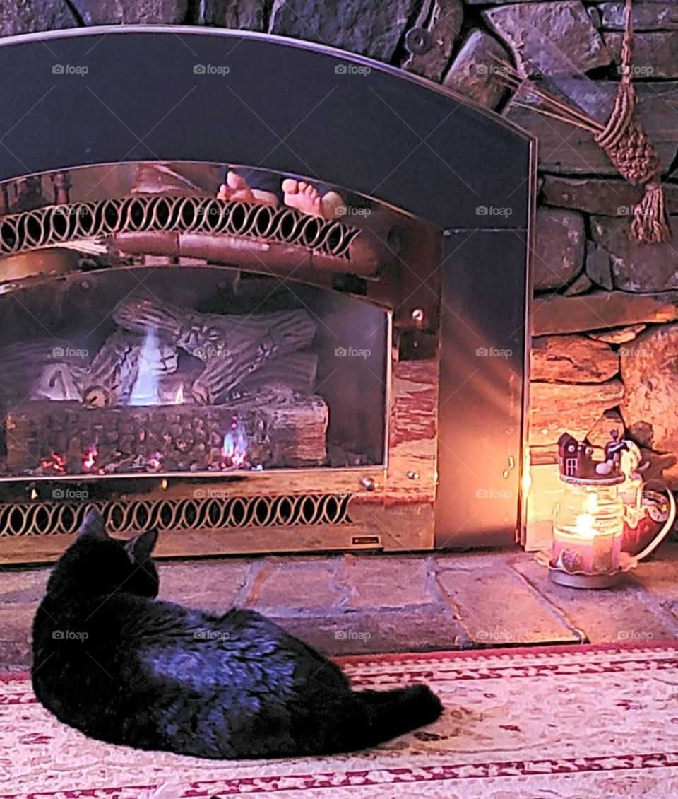 Photo of black kitty laying in front of fireplace keeping her warm. This is a relaxing picture & peaceful to look at.