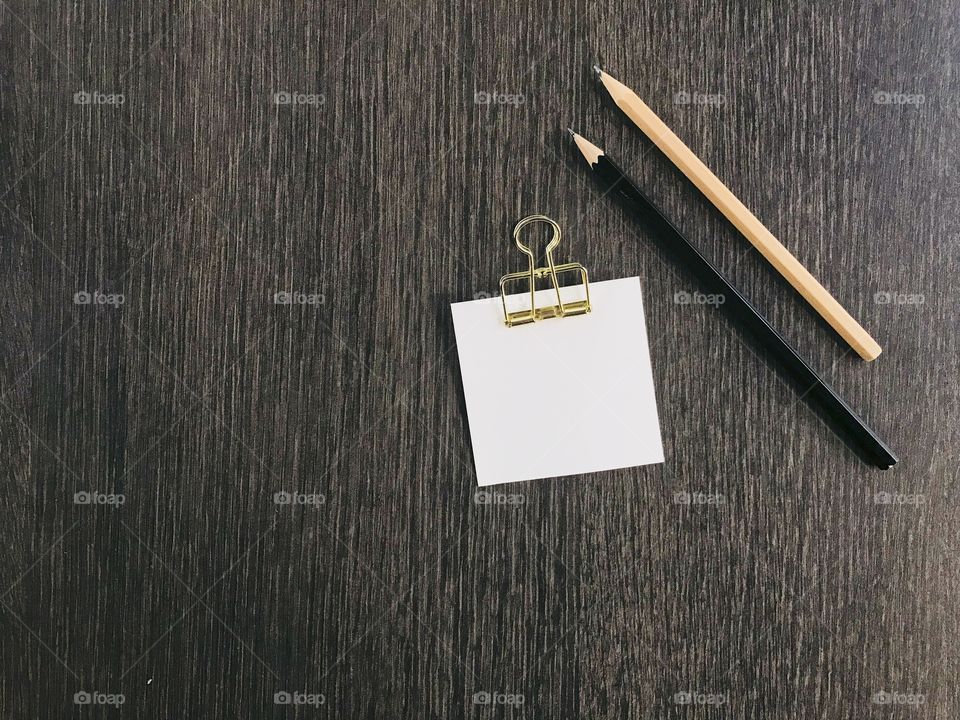 white note paper with golden clip on it and black and brown pencils put on dark brown table with copy space on left side of frame