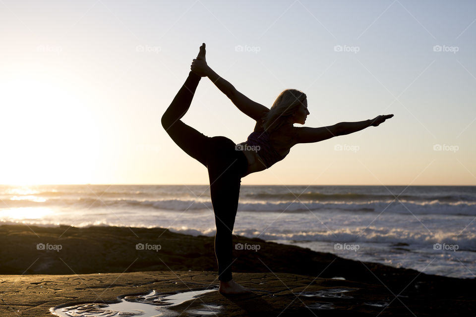Silhouette of woman doing yoga pose on the beach at sunset. 