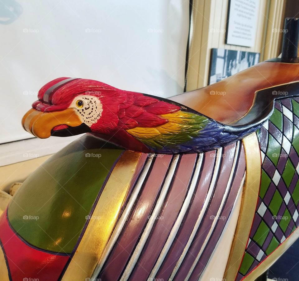 Colorful carved wood parrot on the back of the saddle of a carousel horse in a museum in Sandusky, Ohio