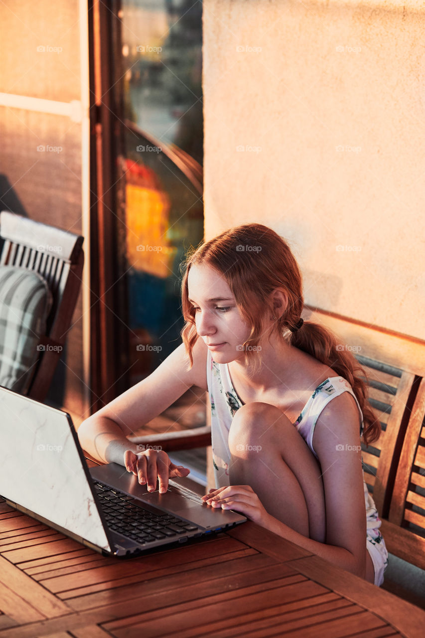 Woman working at home, using portable computer, sitting on patio on summer day. Candid people, real moments, authentic situations