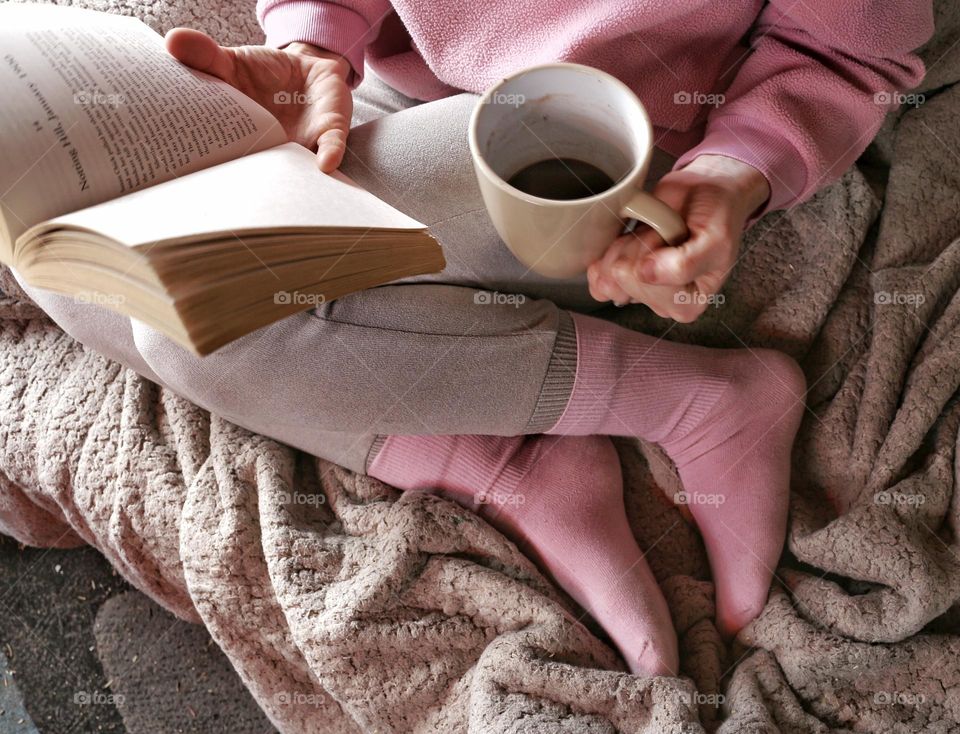 Cuddled up with a book and a cup of coffee wearing baby pink socks and sweater.