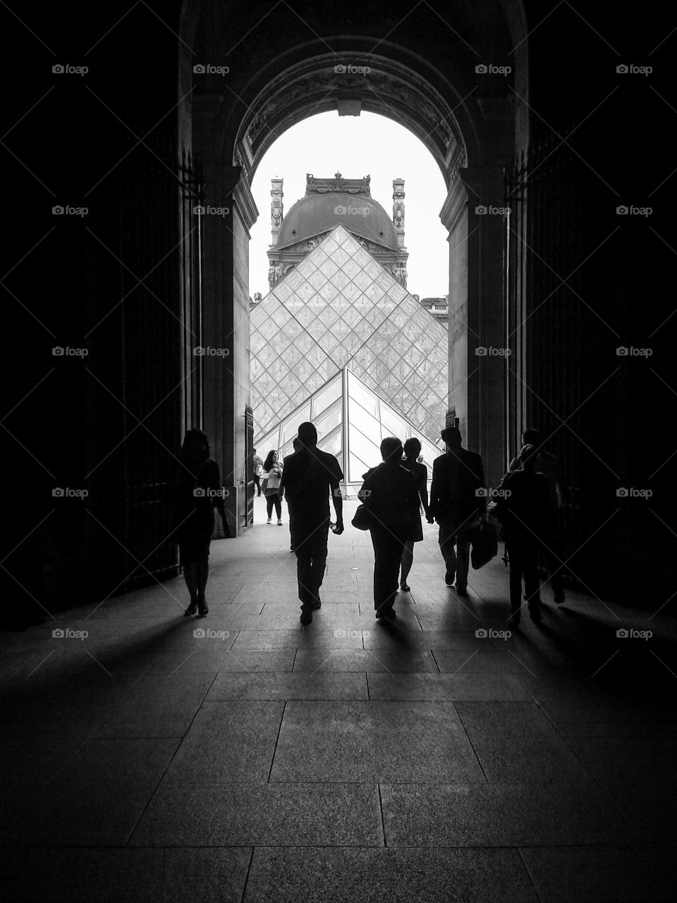 visiting Paris.. tourits seen as silhouette walking under a door in the Louvre museum in Paris- France leading to the Louvre pyramid.