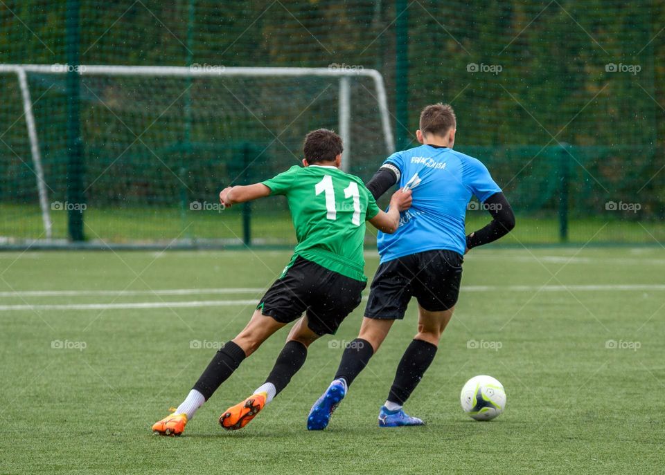 Rear view of two youth players battling for ball while playing an official football match