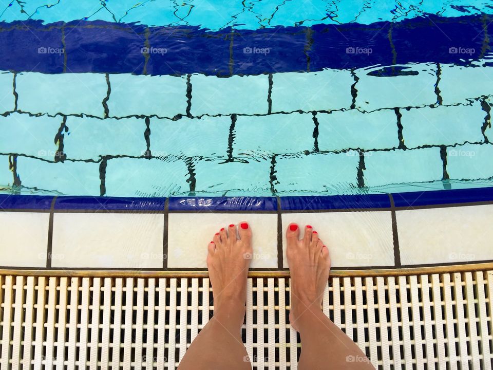 Woman's feet with red nails by the pool ready to get into the water