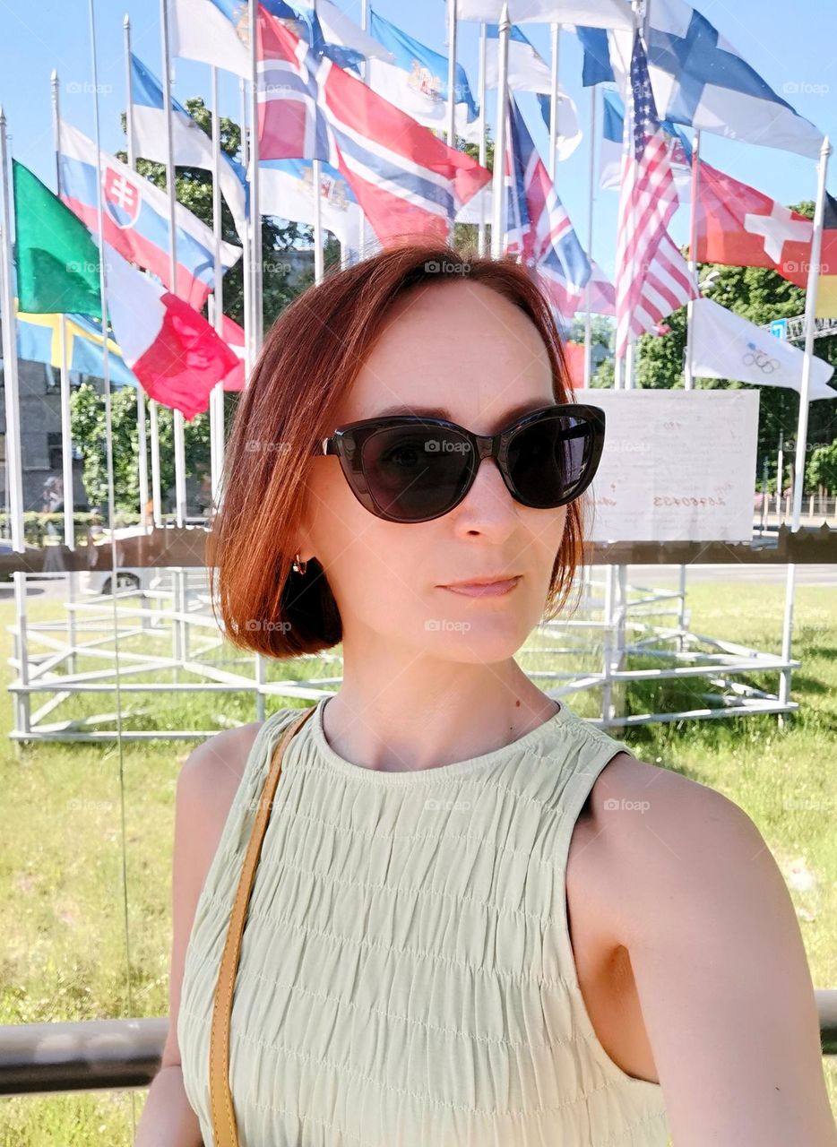 Woman selfie, summer in the city. Against the background of international flags.
