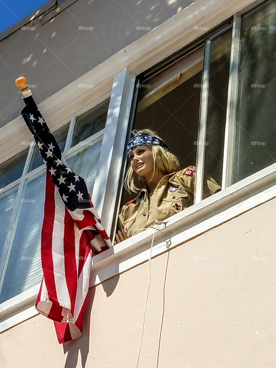 Mannequin dressed as a scout hoisting the American flag out the window for July 4th