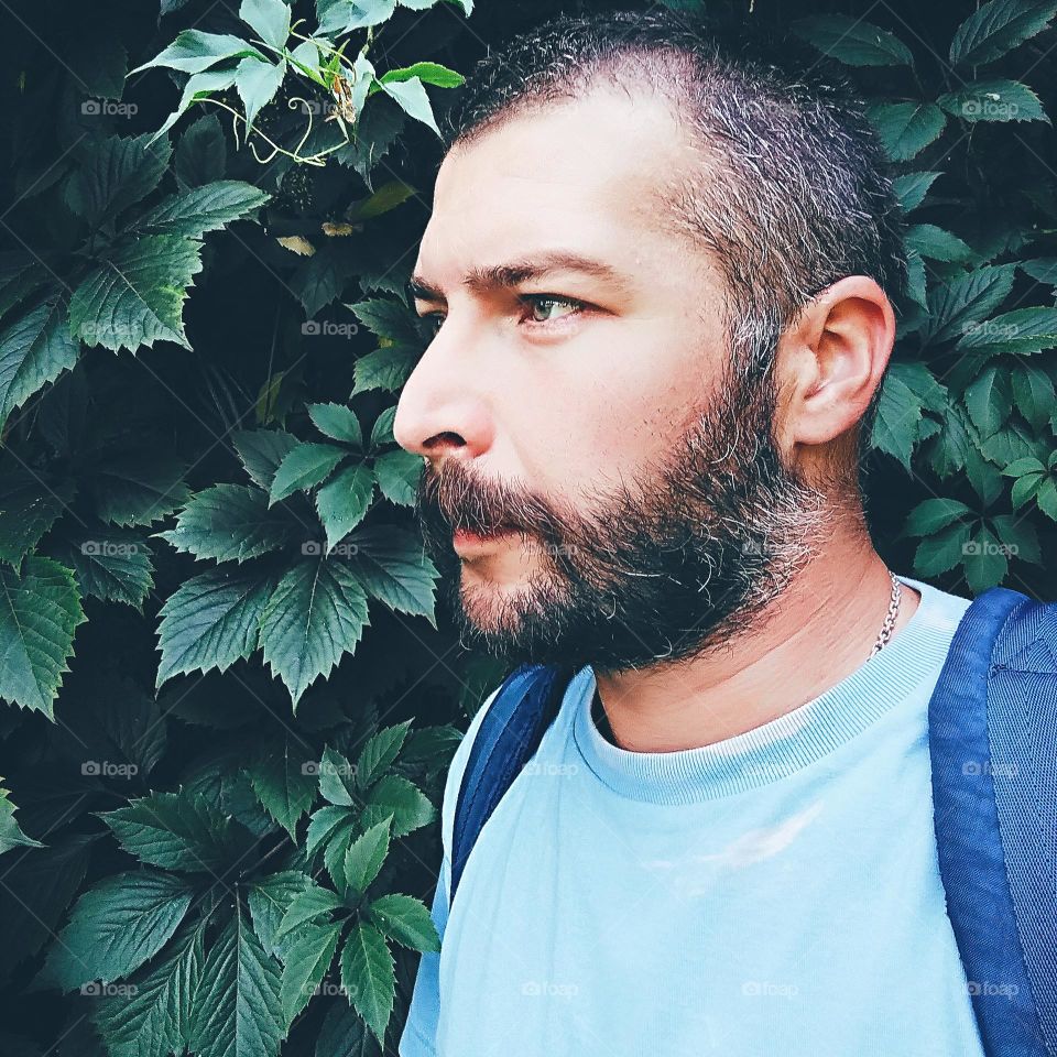 a man with a beard on a background of green leaves of a vineyard