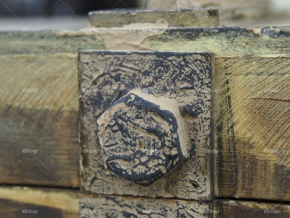 A rusted old bolt with paint flaked off on a wooden antique looking trunk. 
