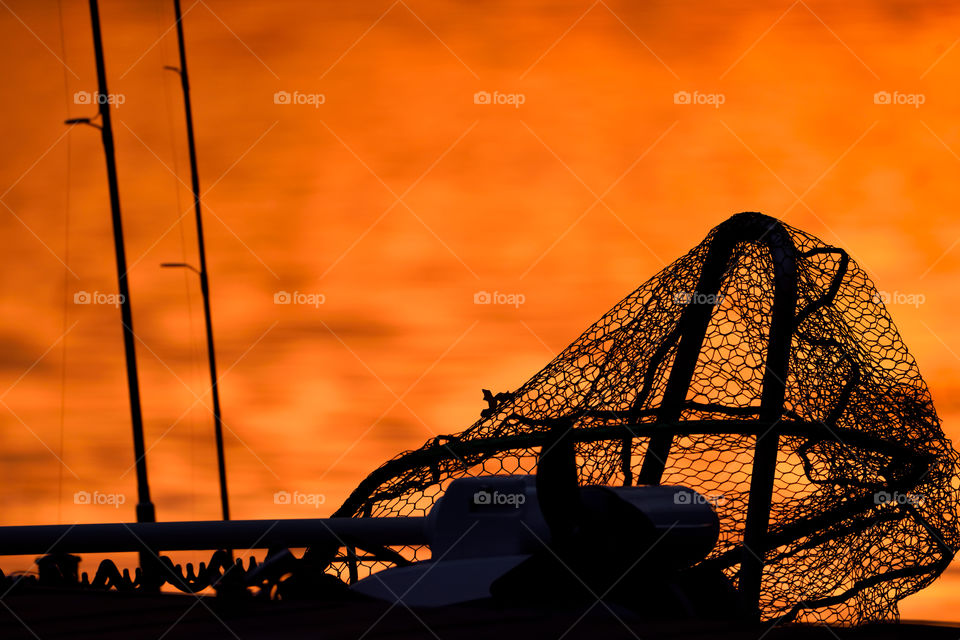 Silhouette of a trollingmotor, landing net and fishing rods
