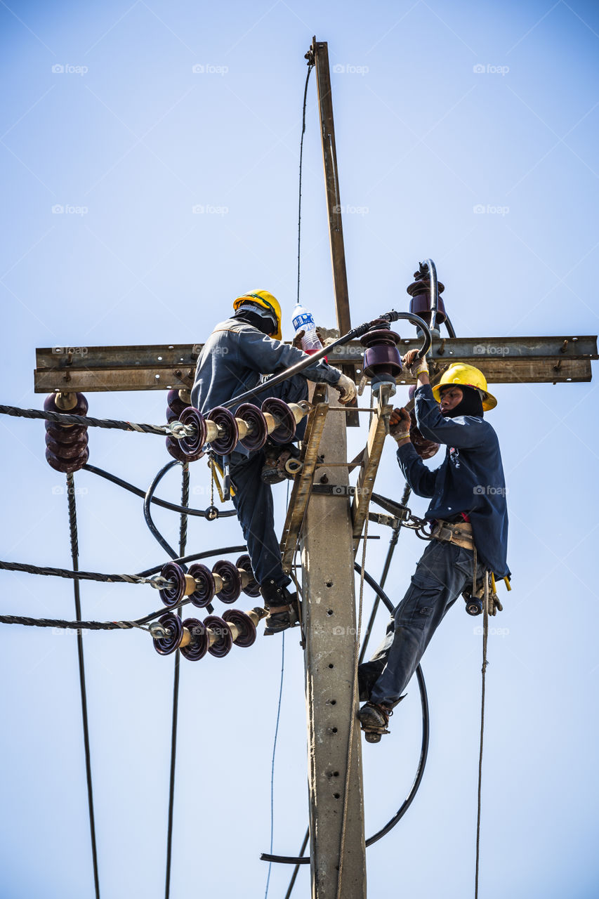 Electrician resting while working on the electricity pole to replace the electrical insulator