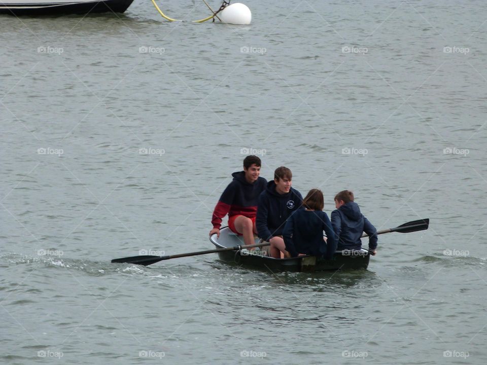 Young men row with a smile to bring their dinghy to the boat. Friendship between men is about combining strengths to move forward while having fun.