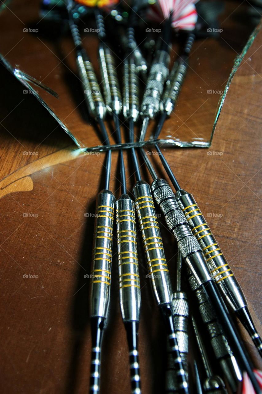 Darts are reflected in a piece of broken mirror on a wooden table 