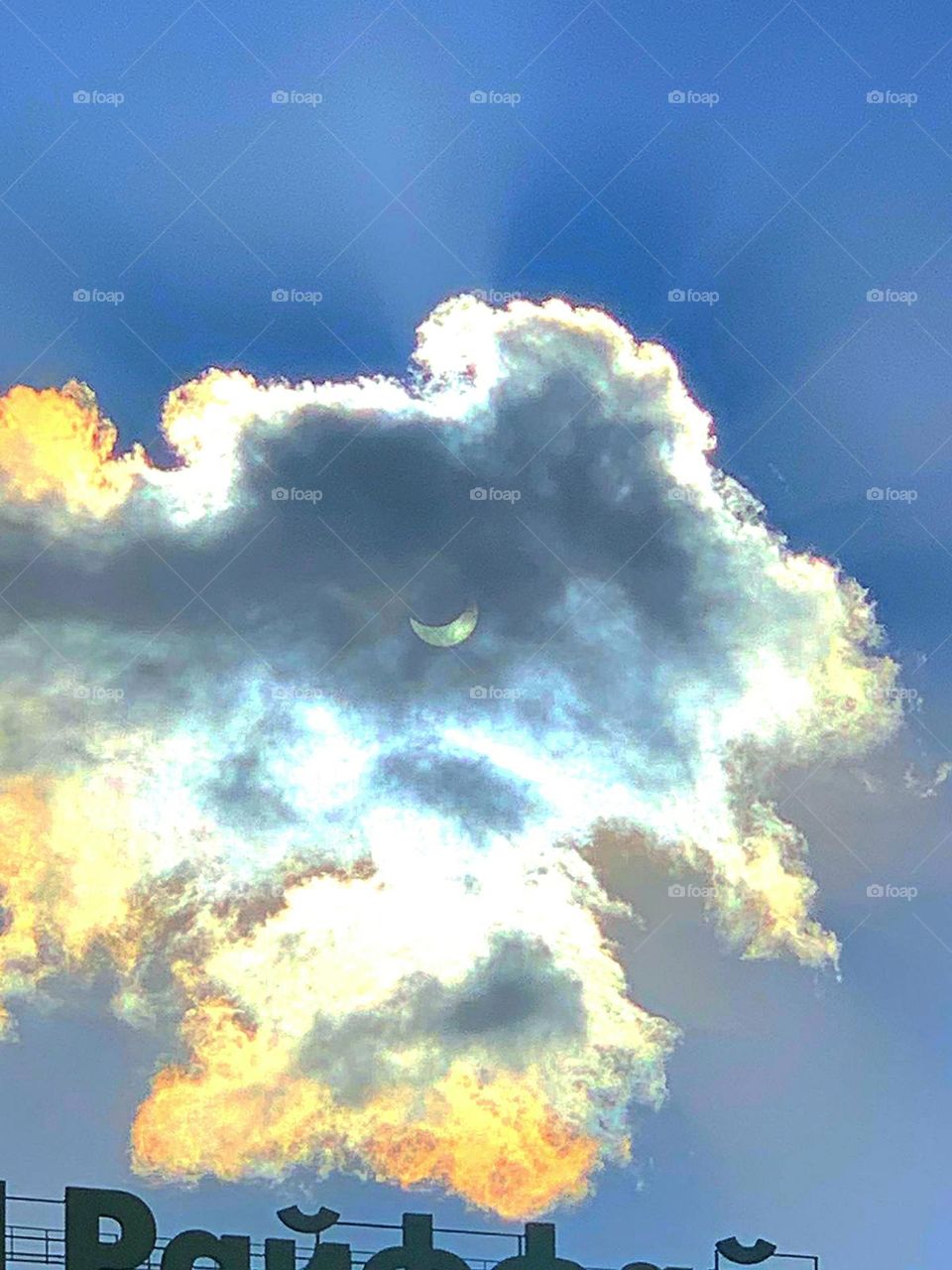 Cloud.  Solar eclipse.  Through the cloud you can see the sun, which the moon covered by 70 percent.  The remaining sun spreads its rays and colors the blue sky and cloud