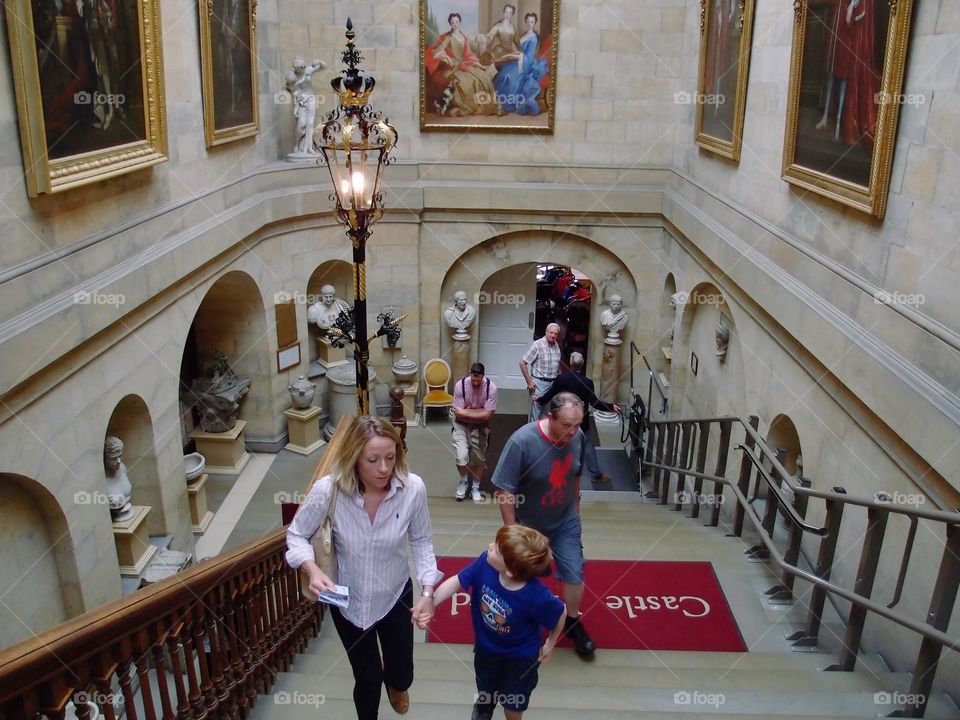 A mother and son hold hands as they climb a stairway to explore Castle Howard in England together. 