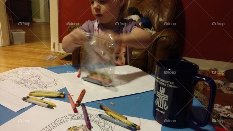 Young little girl coloring bright colors with crayons in her pajamas during breakfast.