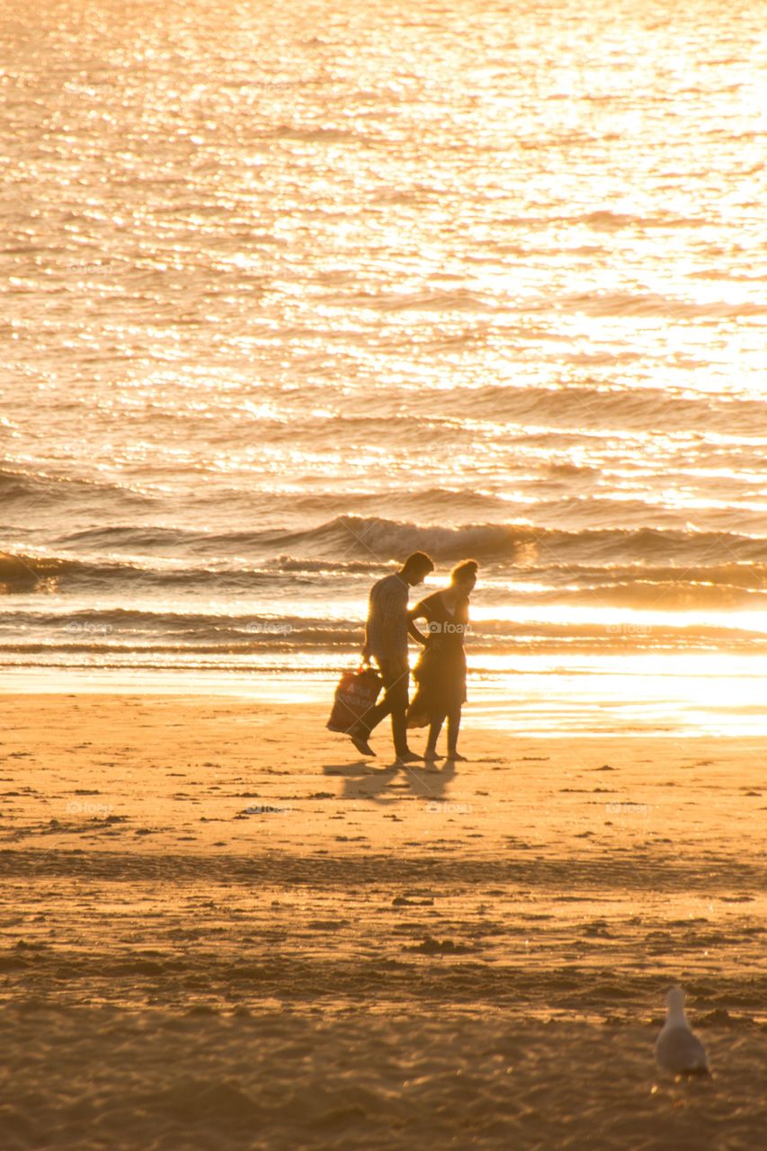 Two people walking hand in hand over the beach during a beautiful sunset