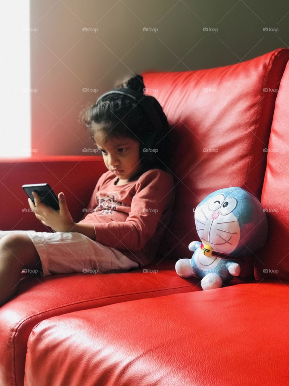 Baby girl watching phone by sitting on red couch alone with her favourite toy beside her😍