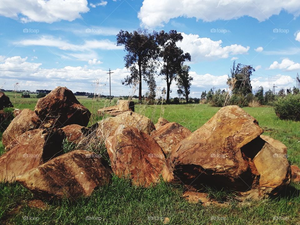 A beautiful rock, trees and cloudy skies at the farmland.