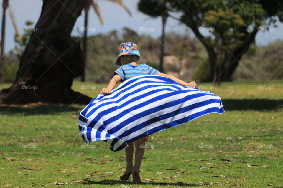 Little boy running across grass pretending his beach towel is a cape 