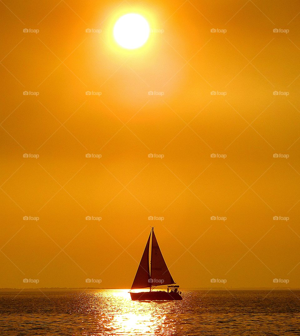 
Memories of summer - Sailing in the golden sunset. A swift running sailboat maneuvers  its way across the calm waters of the bay during a colorful, golden sunset
