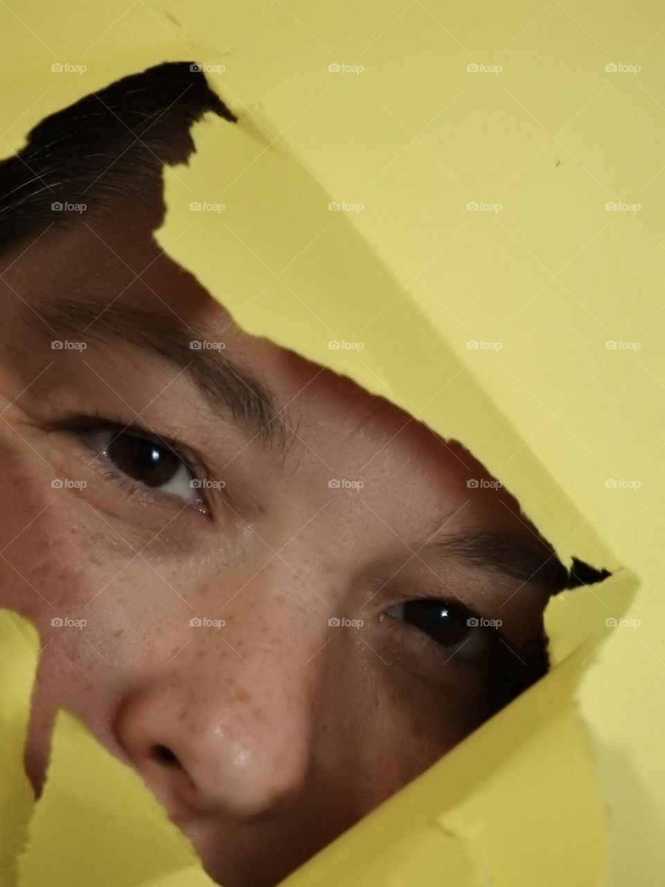 Face skin in the forties of a woman with freckles and brown hair seen through a broken yellow paper.