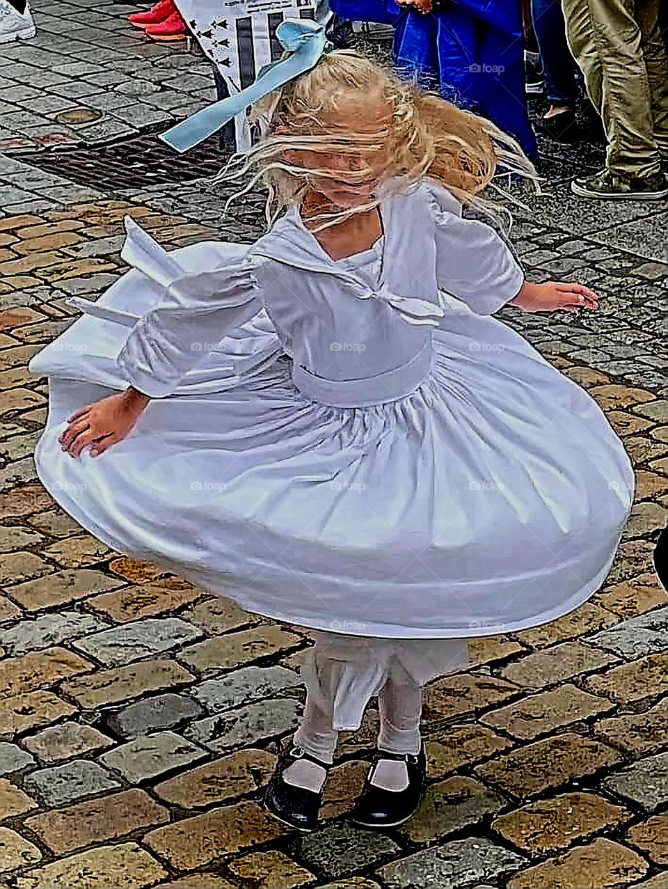 Young blond girl dressed in a white Breton traditional costume dancing and twirling in a street of Quimper at the Cornouaille Festival