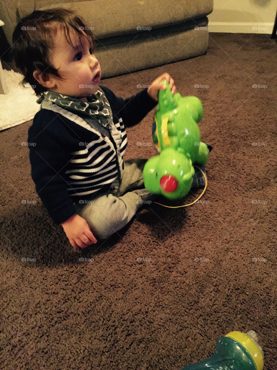 Baby on the floor with his bright green dinnasour toy. 