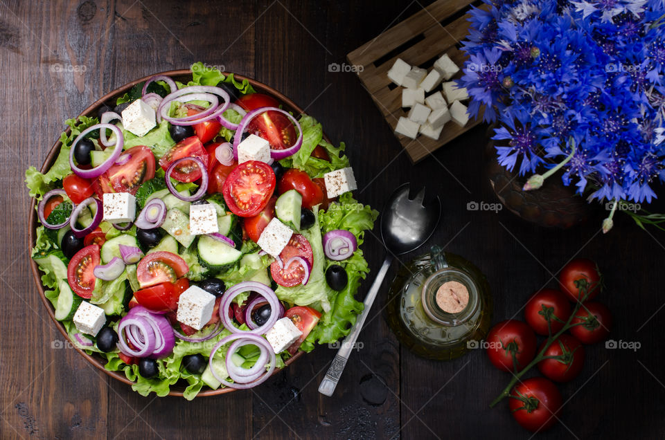Greek salad on brown plate with ingredients on dark background