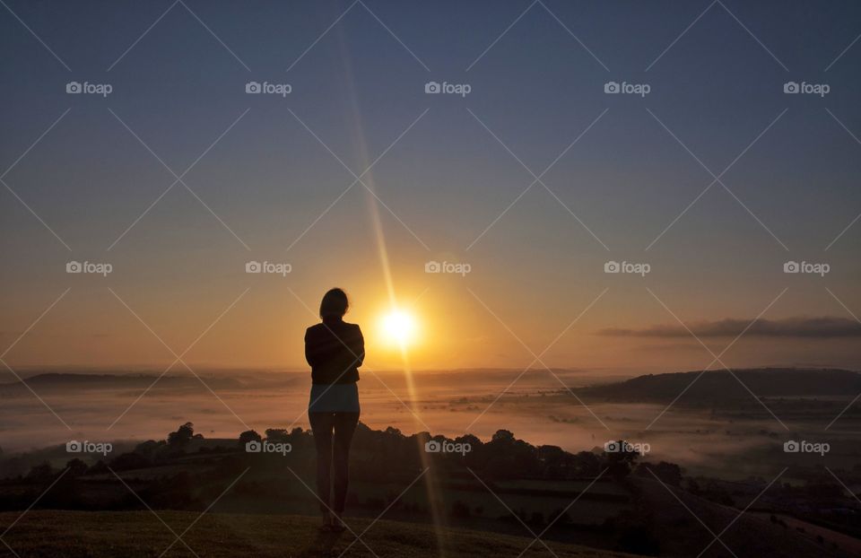woman watching sunrise ovef Glastonbury hill in England