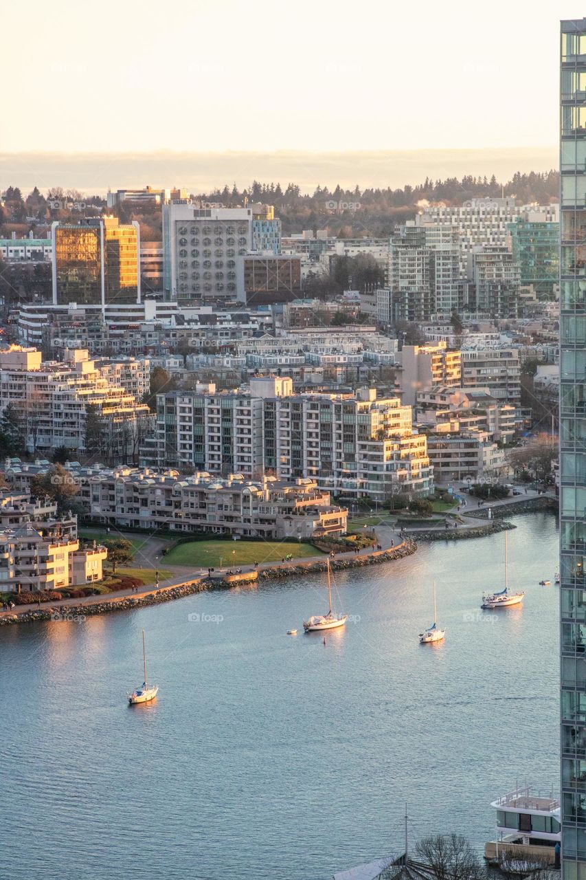 Small boats in a river going through a city with tall buildings at sunset.