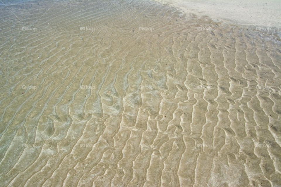 Sand’s surface patterned with ripples left by waves on the virgin beach