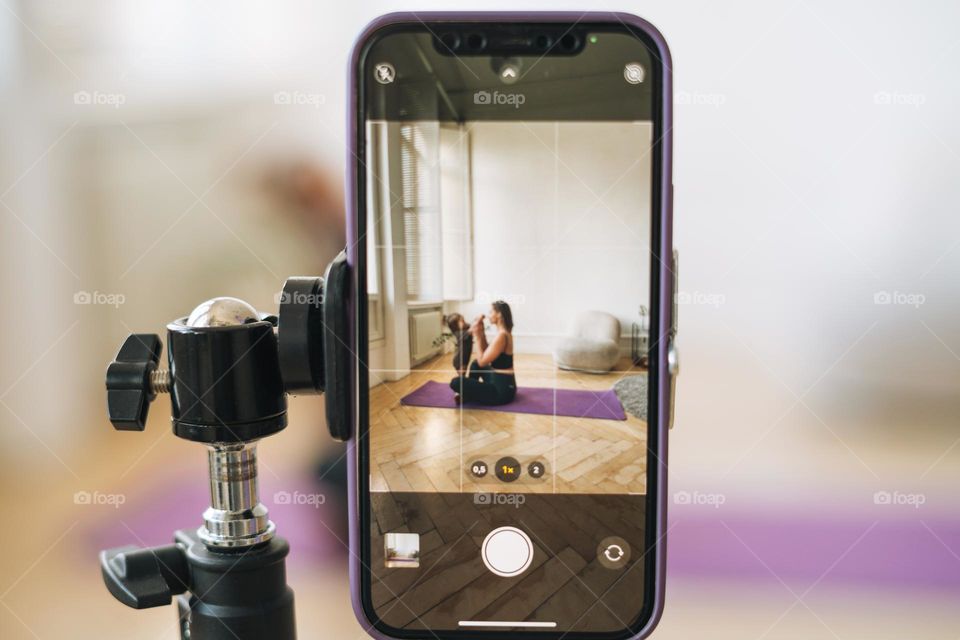 Young woman with little daughter fitness blogger doing exercises and recording video on mobile phone in studio