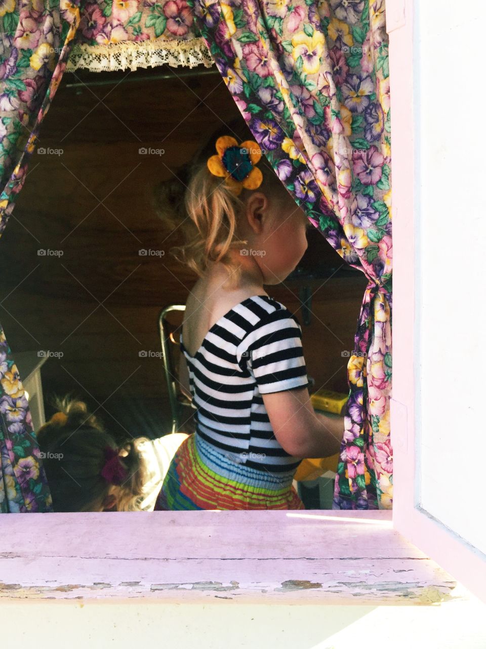 Blonde little girl with pigtails whimsically dressed viewed through playhouse window