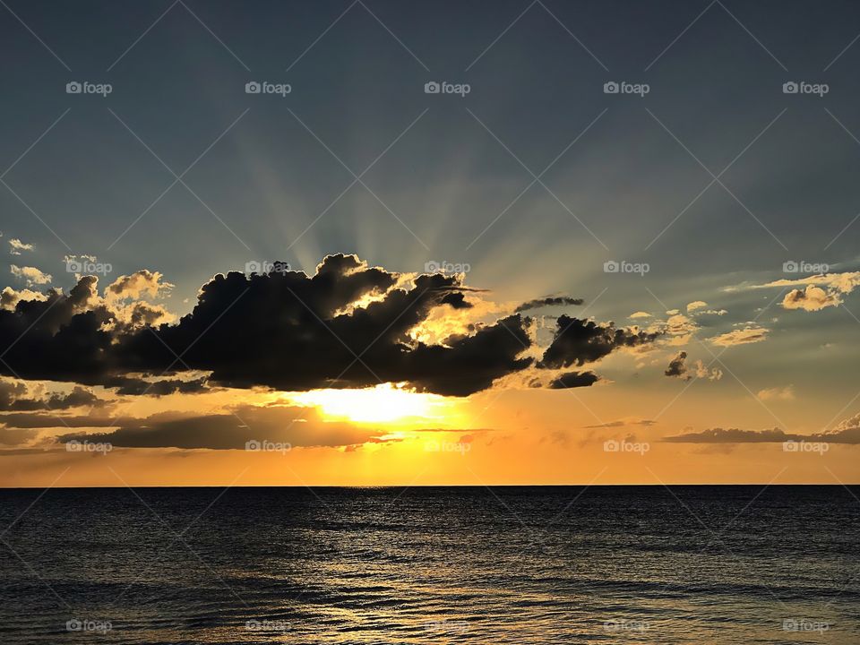 Black clouds contrast with the golden rays of an ocean sunset.