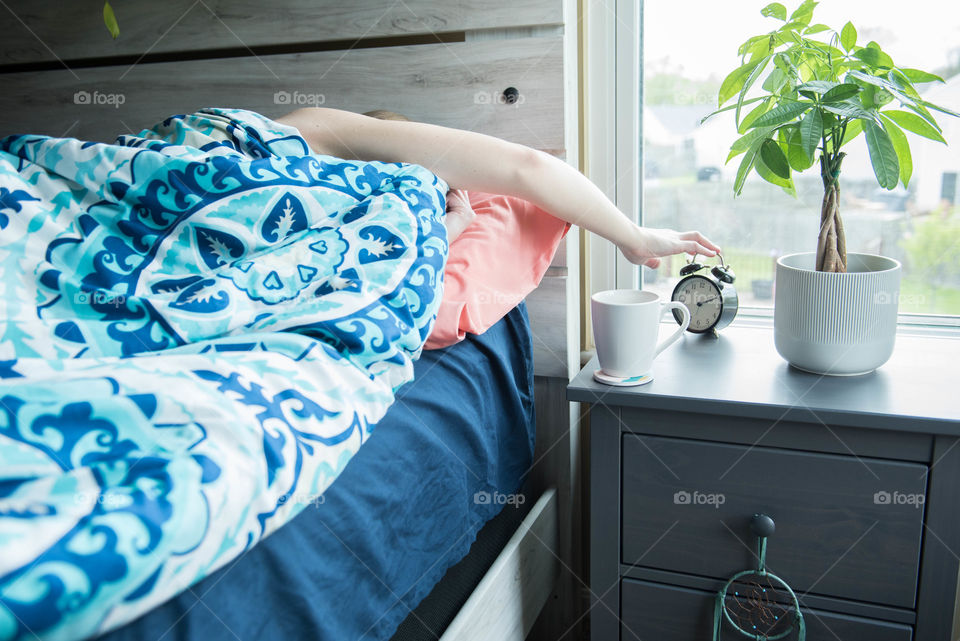 Woman lying in bed the morning and reaching over to turn off an alarm clock